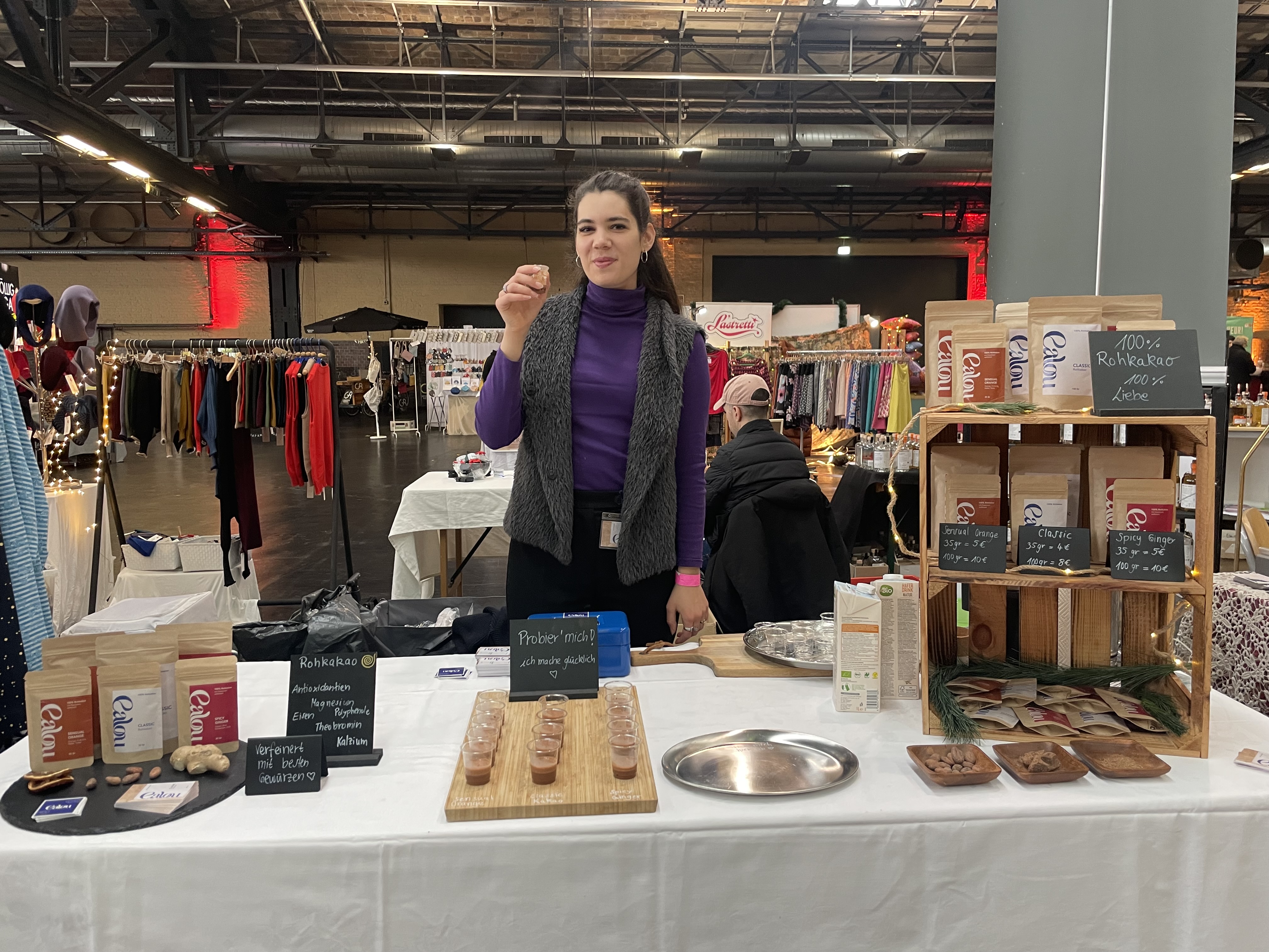 Emmalou behind a market stand with Calou Kakao products and tasting cups.