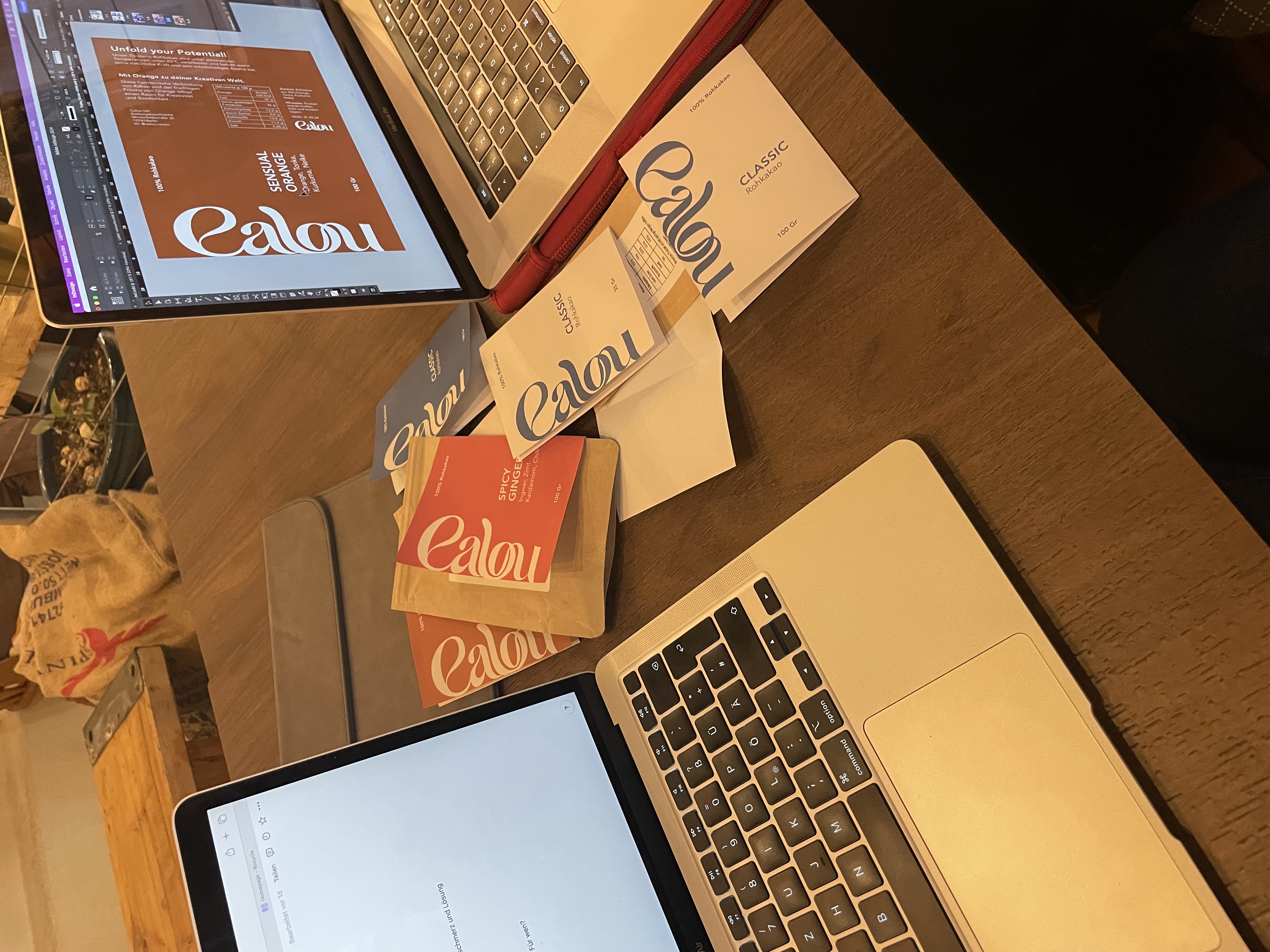 Calou packaging designs on a laptop beside printed labels and cacao pouches.